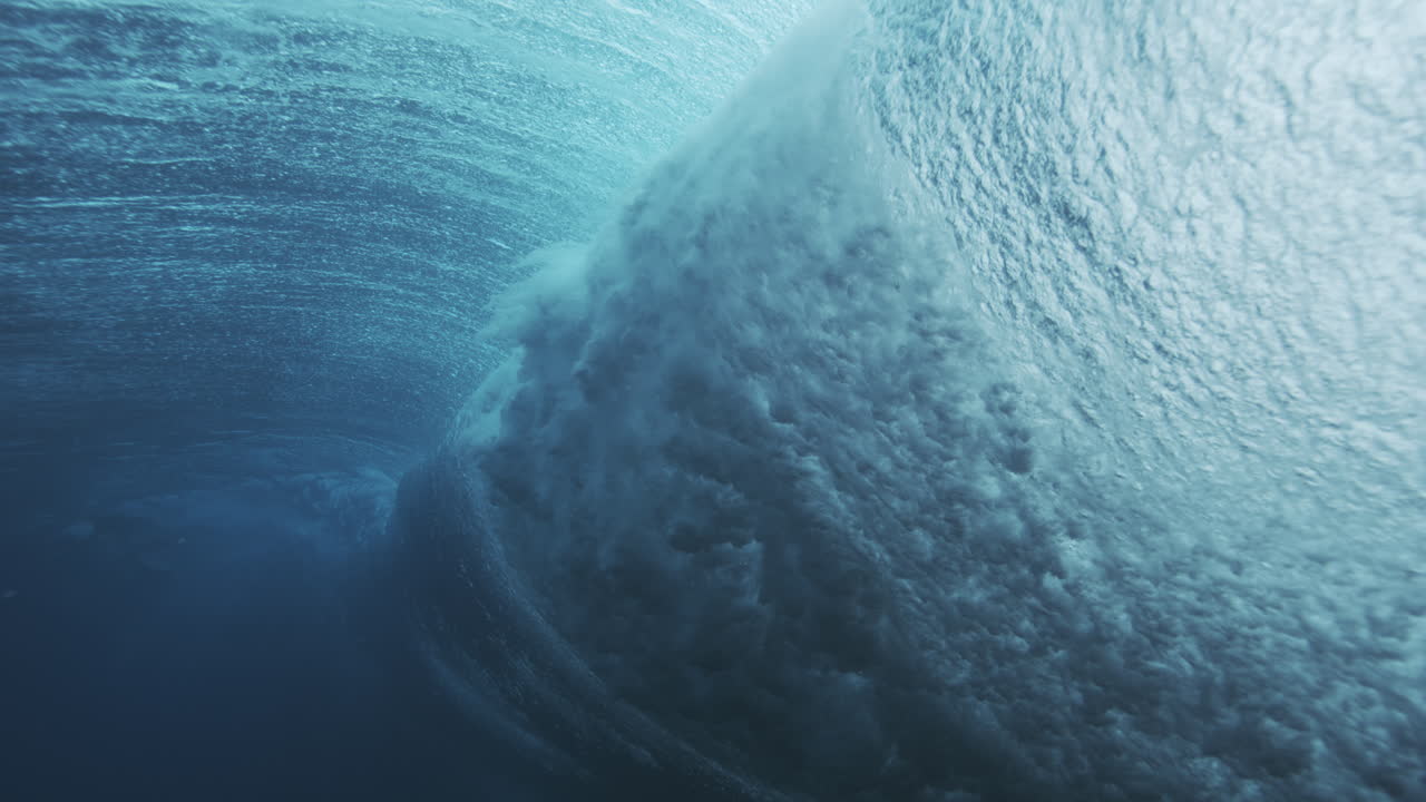 Underwater wave face with textured surface and rolling motion in deep blue ocean water