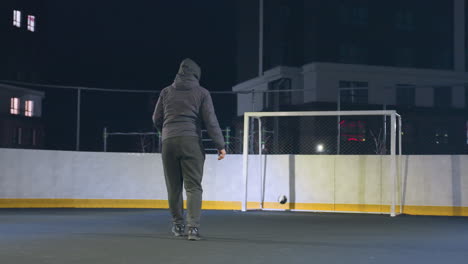 athlete kicks soccer ball toward goalpost during night training on urban outdoor field as ball bounces out, illuminated backdrop and dynamic motion create an atmosphere of focus