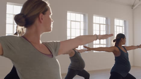 yoga-class-of-healthy-pregnant-women-practicing-warrior-pose-enjoying-group-physical-fitness-workout-with-instructor-in-studio-at-sunrise