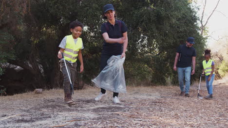 adult team leaders with group of children at outdoor activity camp collecting litter together