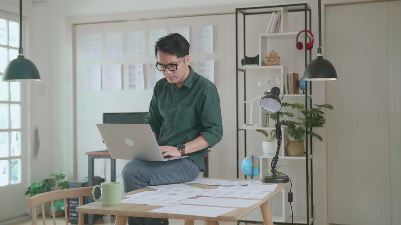 Creative Designer Sits On His Desk Holds Laptop On The Knees And Working On The Project . Creative Design And Gaming Content Development Studio
