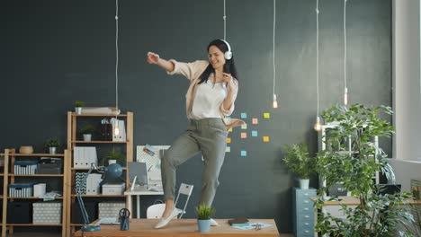 mujer de negocios feliz bailando en el escritorio de la oficina haciendo tonterías disfrutando de la música en los auriculares