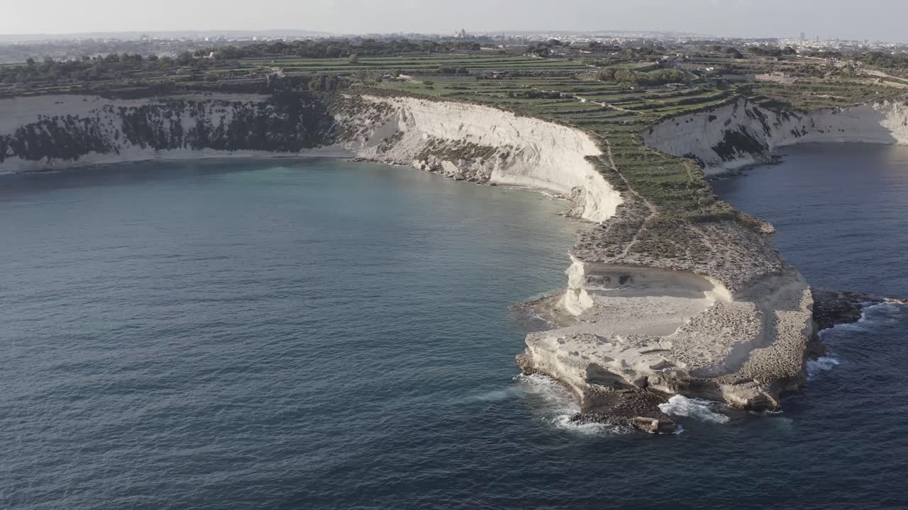 A drone circles the monumental cliffs of Ras il-Fenek, capturing sheer limestone walls and the endless blue expanse of the Mediterranean Sea
