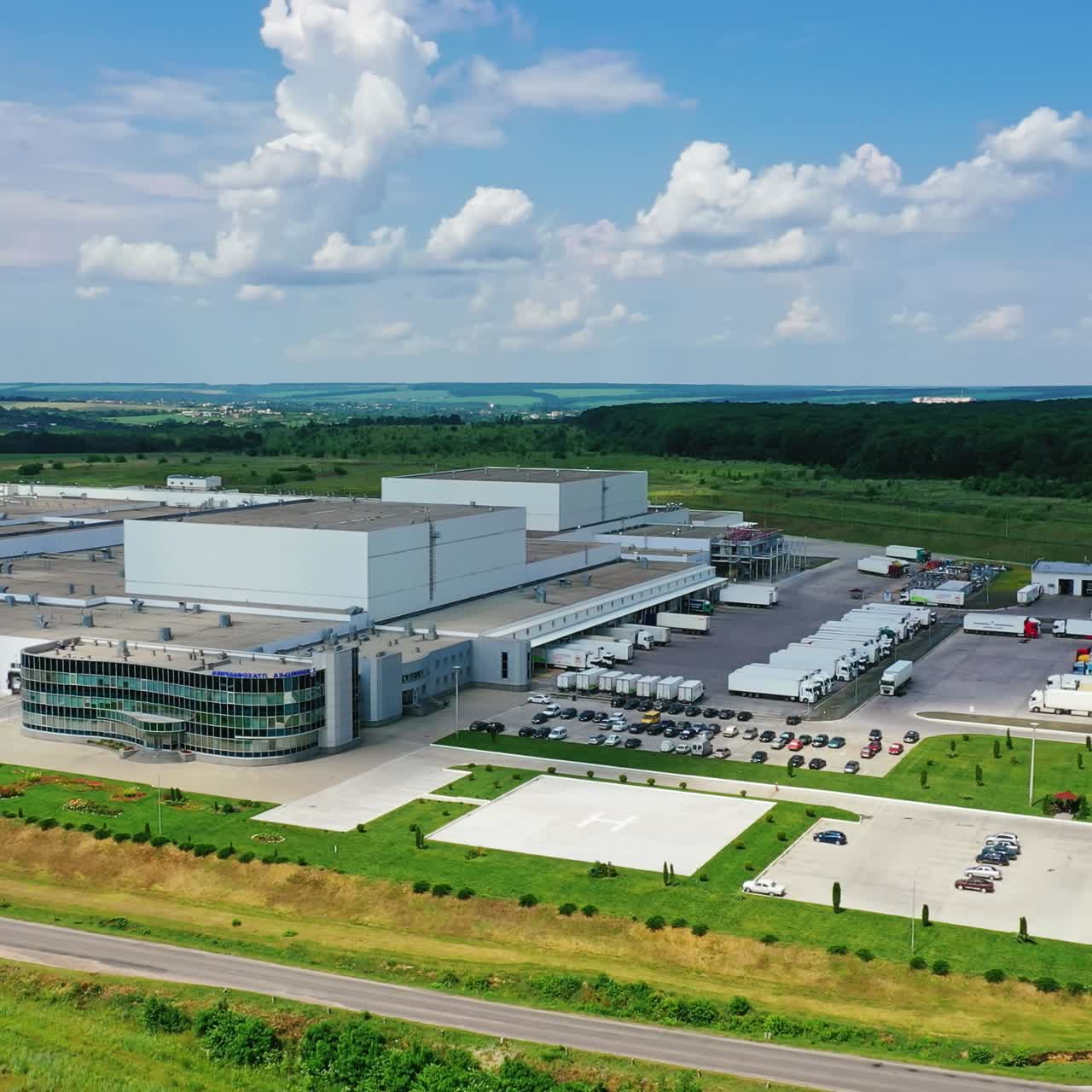 Exterior of modern factory in rural place. Innovative complex with car parking on green nature background. Industrial zone on fields. Aerial view.