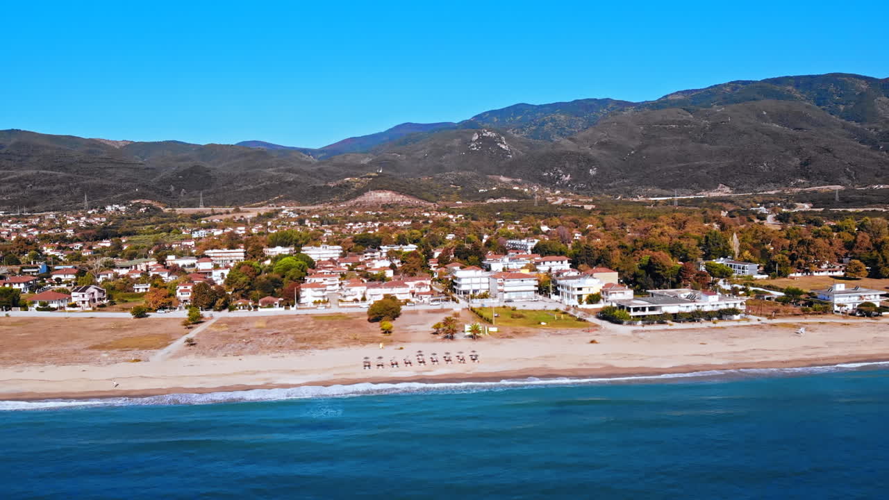Panorama of the Asprovalta with buildings and greenery, green hills. Long beach with umbrellas and sunbeds. Sunny day. Greece