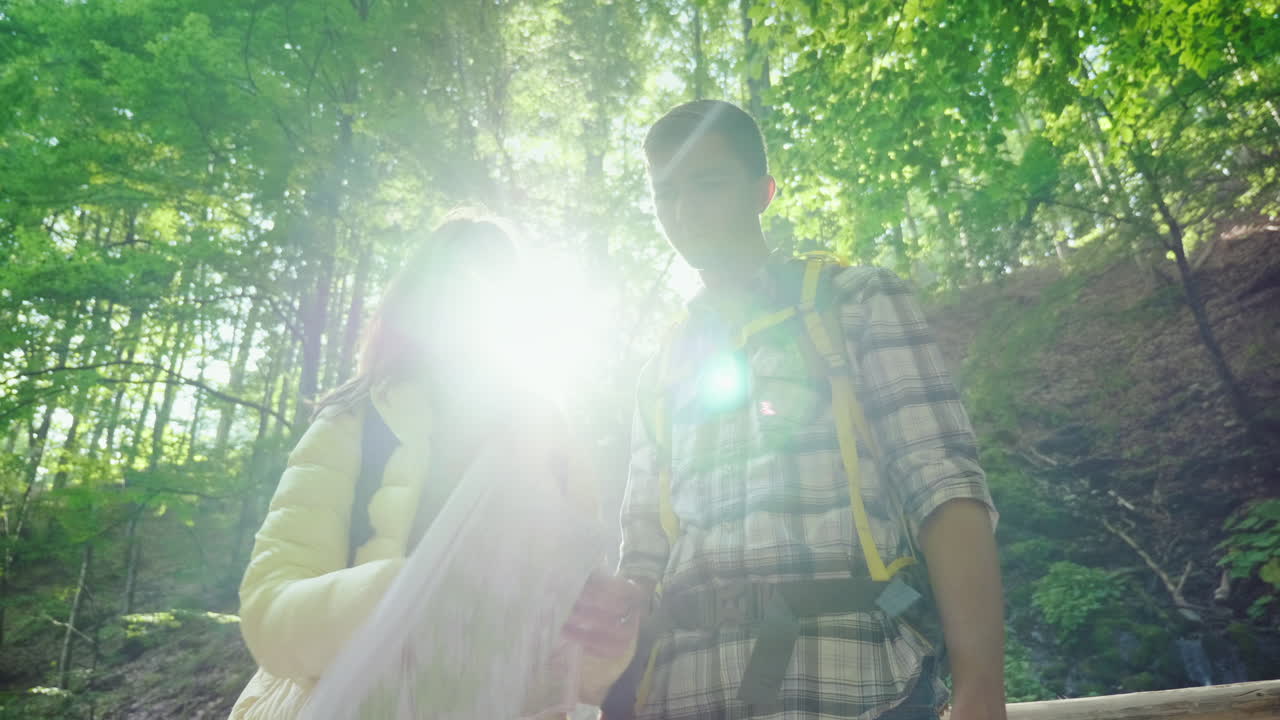 una pareja joven de turistas mirando un mapa se paran en los rayos del sol en el bosque cerca del