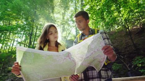 a young couple of tourists looking at a map they stand in the rays of the sun in the forest near the