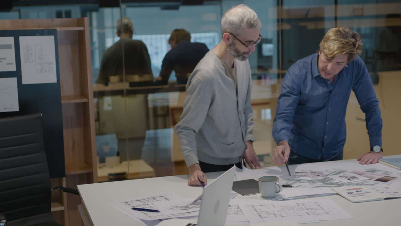 Seniorarkitekt diskuterer plantegning med mannlig kollega på kontoret