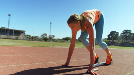 Seitenansicht-Einer-Kaukasischen-Sportlerin,-Die-Die-Startposition-Einnimmt-Und-Auf-Einer-Laufstrecke-Bei-Spo-Läuft