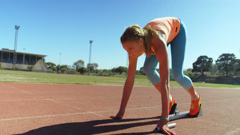 vista lateral de una atleta caucásica tomando la posición inicial y corriendo en una pista de correr en spo