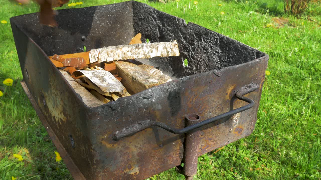 젊은 남자가 나무 통나무를 내려놓고 베이킹과 바비큐를 위해 녹슨 그릴을 준비하고, 중간 클로즈업 샷