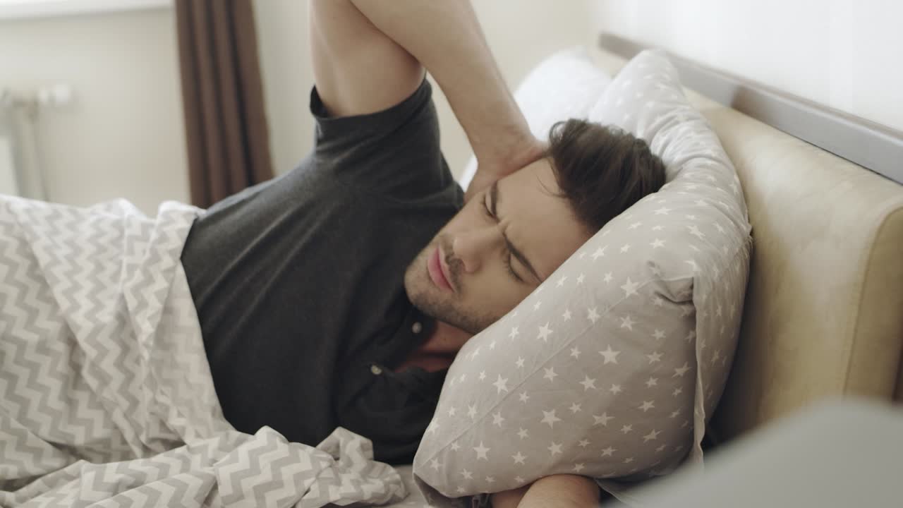 hombre soñoliento que odia el ruido del despertador. hombre enojado que cubre la cabeza con una almohada.