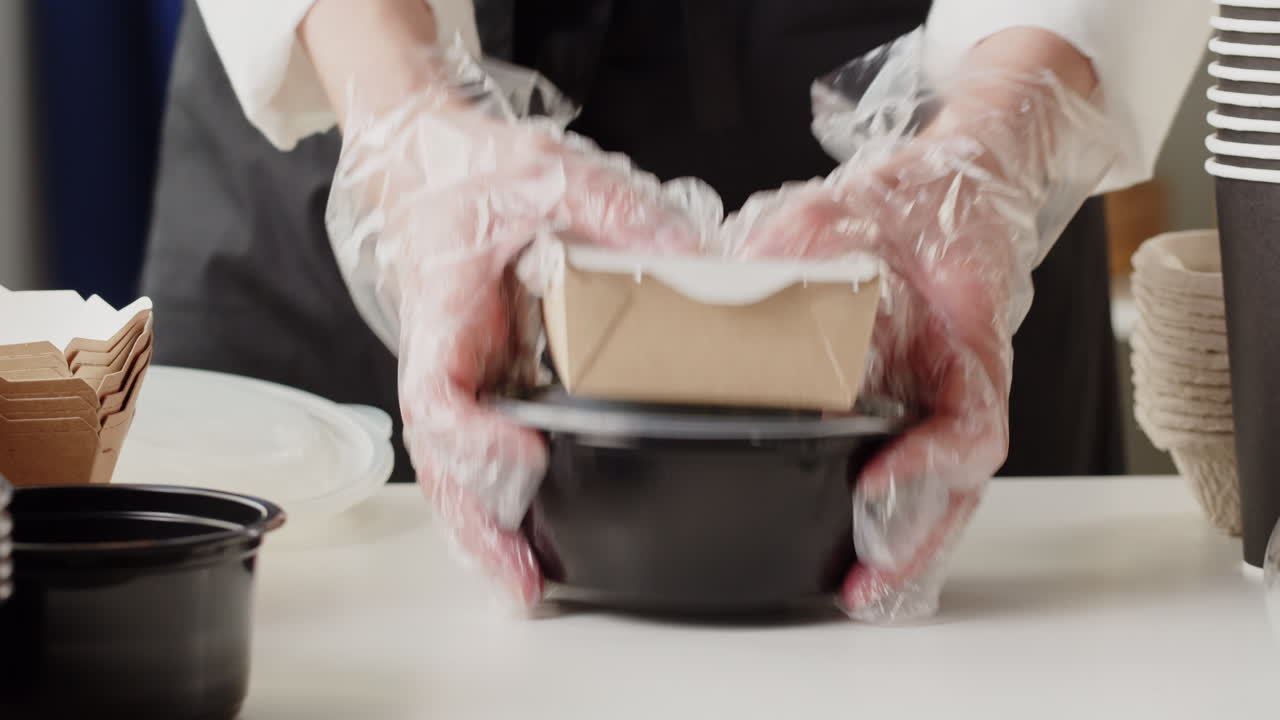 Mani in guanti che confezionano cibo da asporto in contenitori monouso