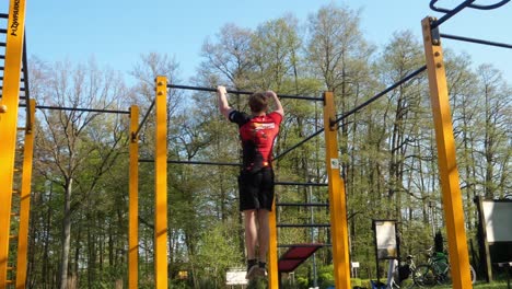 white man jump and muscle up on exercising bar in outside gym wide