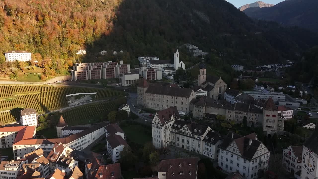 Aerial view of the historic city of Chur, Switzerland, bathed in the warm light of the setting sun. The iconic Cathedral of St. Lucius dominates the skyline, adding to the city's charm and history.