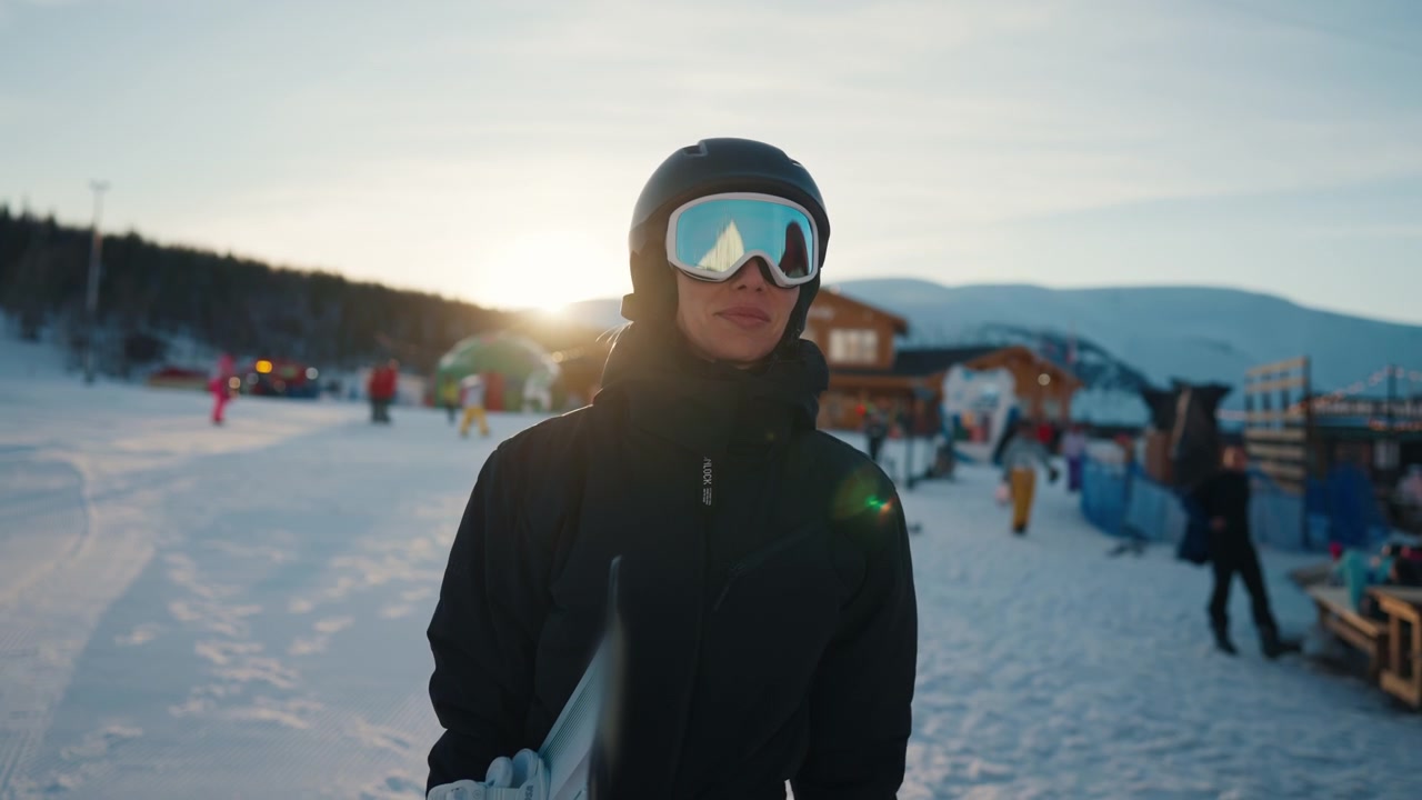 Giovane donna che tiene uno snowboard in una stazione sciistica al tramonto