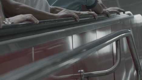 a medium shot of multiple people going up an escalator, captured with a static camera, showing only arms and hands in focus