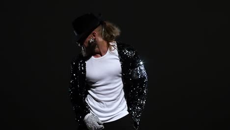 man in sequin jacket and hat dancing on a dark stage