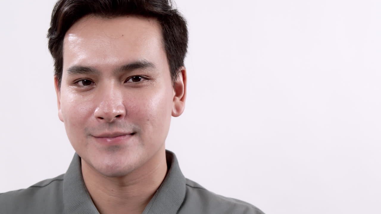 A young man radiates confidence as he smiles gently at the camera, set against a clean white background.