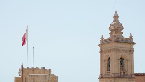 national flag of malta waving in the wind with medieval church bell tower