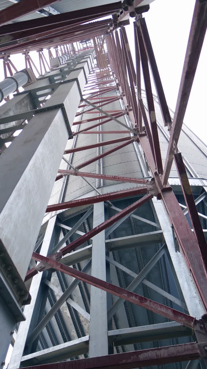 Pipes and supports at the grain-drying complex. High steel constructions at the backdrop of sky. View on the structure from below. Vertical video