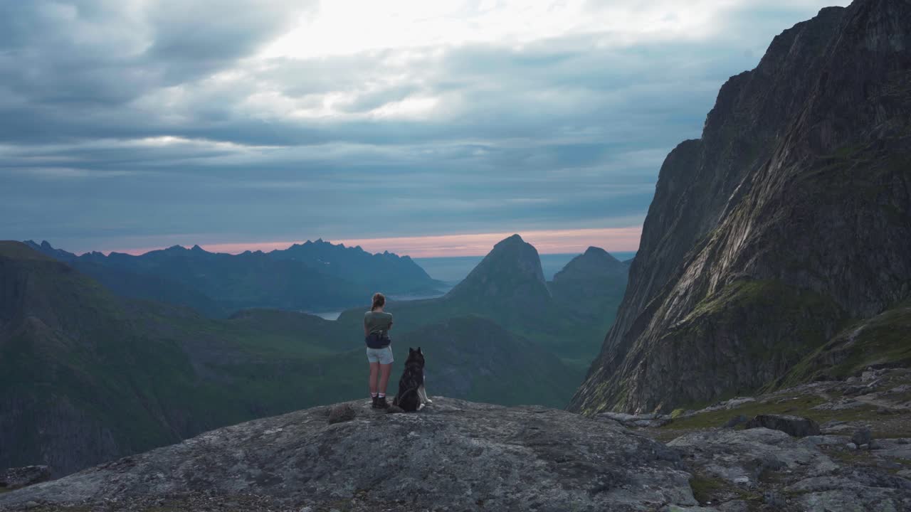 perro sentado al lado de una excursionista filmando el paisaje noruego desde grytetippen al atardecer en noruega