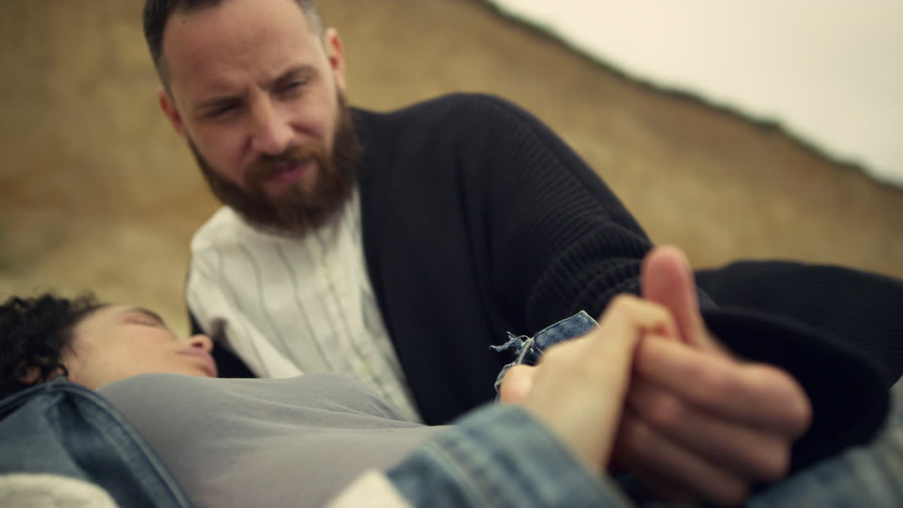 amantes étnicos descansando en la arena de la playa. una pareja romántica tomándose de la mano en una cita relajante.