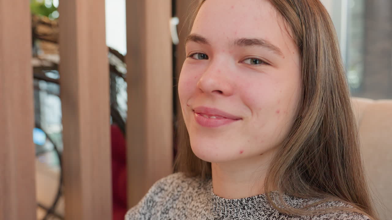 Close-up of cheerful college student seated in eatery, smiling brightly and playfully winking one eye, exuding youthful charm and friendliness in cozy casual indoor setting with blurred background