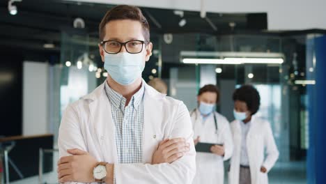 Close-up-view-of-caucasian-male-doctor-in-medical-mask-looking-at-camera-standing-in-hospital