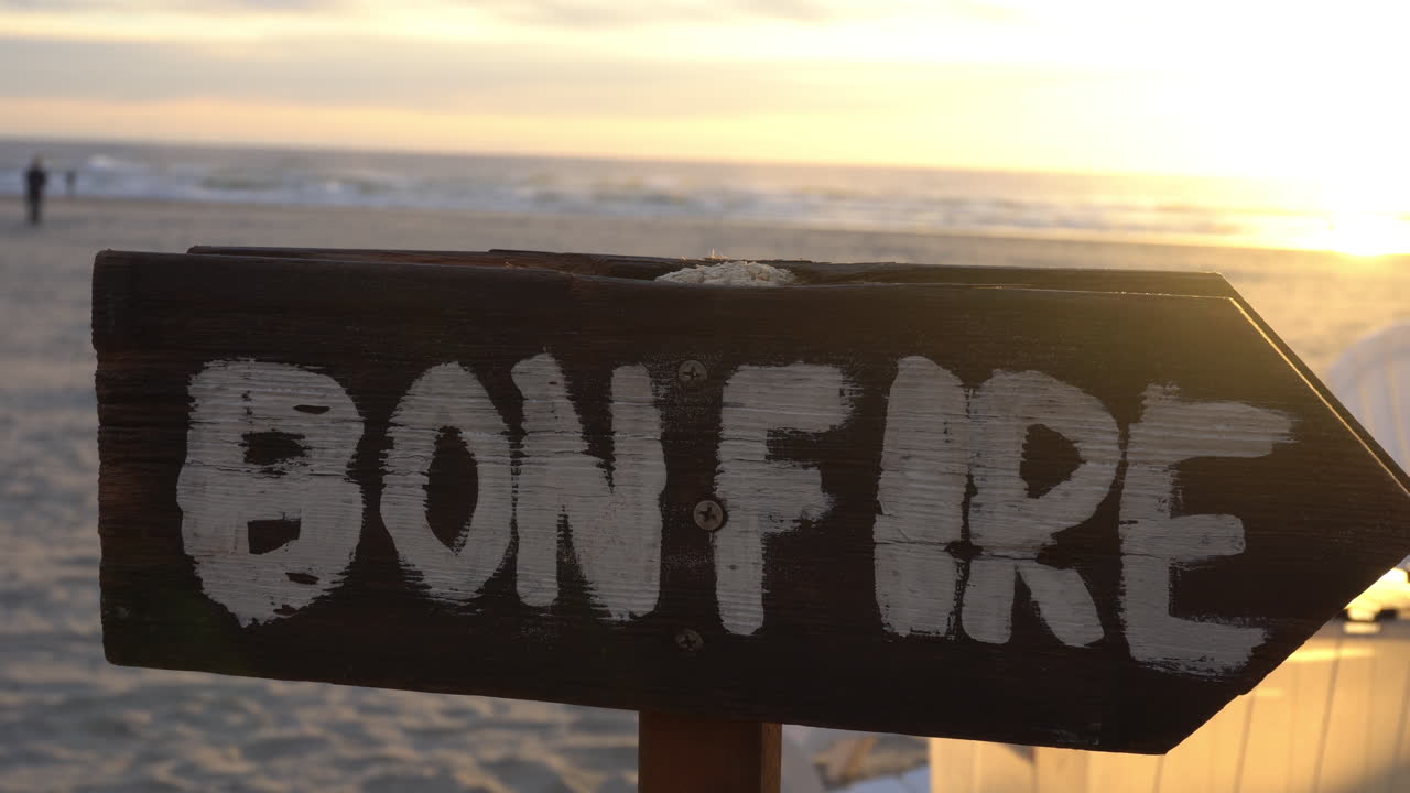 Bonfire sign at the beach pointing to a campfire with the sunset in the background.