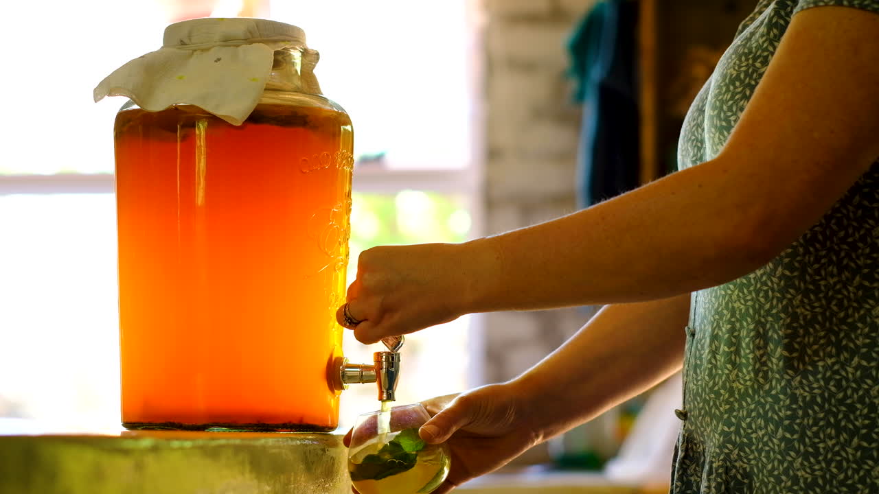 Donna caucasica versa kombucha da un contenitore con rubinetto in un bicchiere