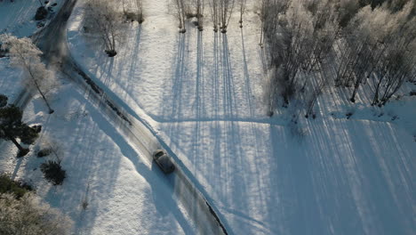 Coche-Conduciendo-Lentamente-Por-Una-Carretera-Helada-Y-Resbaladiza,-Campo-Invernal-Aéreo-Desde-Arriba