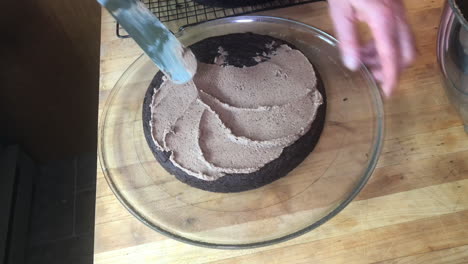 man's hands seen frosting a chocolate cake in a home kitchen