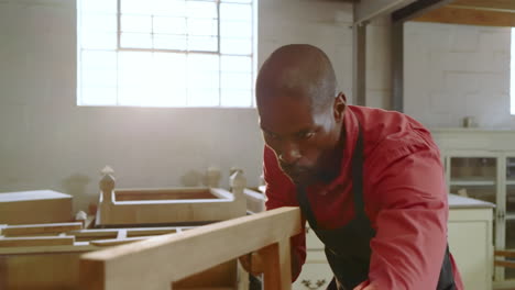 african american man placing frame then sanding beam with block at workbench for smooth finish