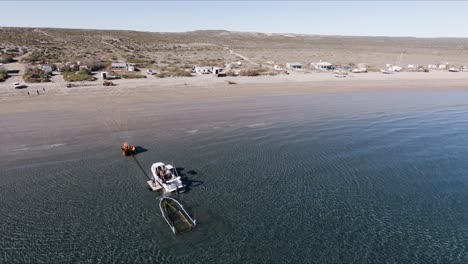 un barco amarrado cerca de la orilla junto a un remolque de barco en el mar descargando su carga - drone aéreo, tiro panorámico