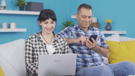 pareja casada pasando el rato en la computadora portátil y el teléfono. uso de la tecnología en casa.