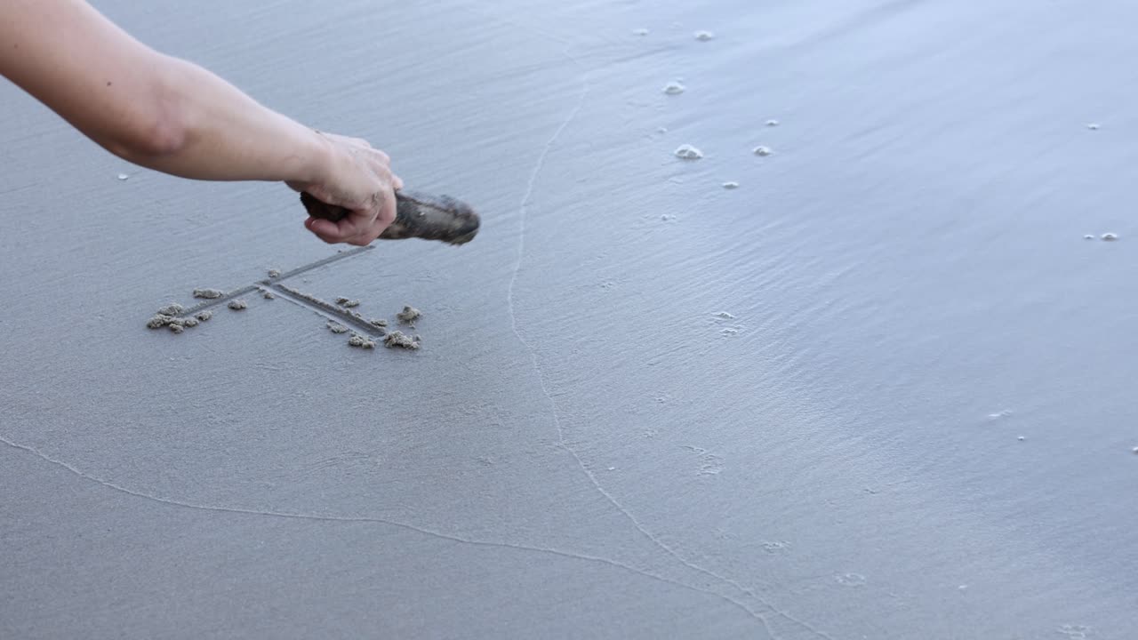 Hand drawing letters on sandy beach.