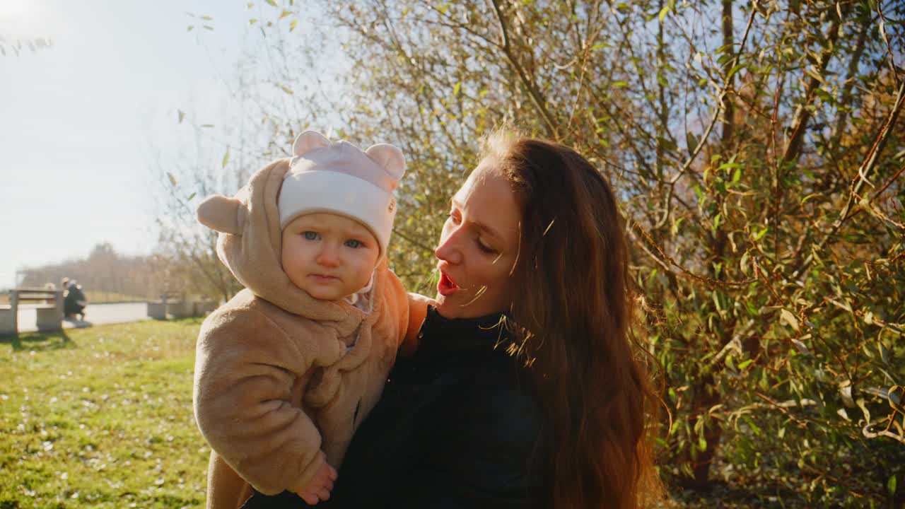 Et gledelig øyeblikk mellom en mor og babyen hennes utendørs, som fanger varmen i båndet deres mot en bakgrunn av natur og mildt sollys