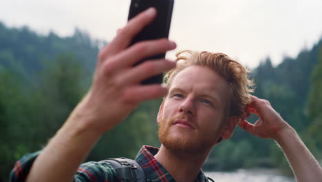 Hombre-Arreglando-El-Peinado-Antes-De-Selfie.-Chico-Tomando-Selfie-En-Teléfono-Inteligente-En-Las-Montañas