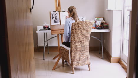 view through door of female teenage artist at easel drawing picture of dog in charcoal