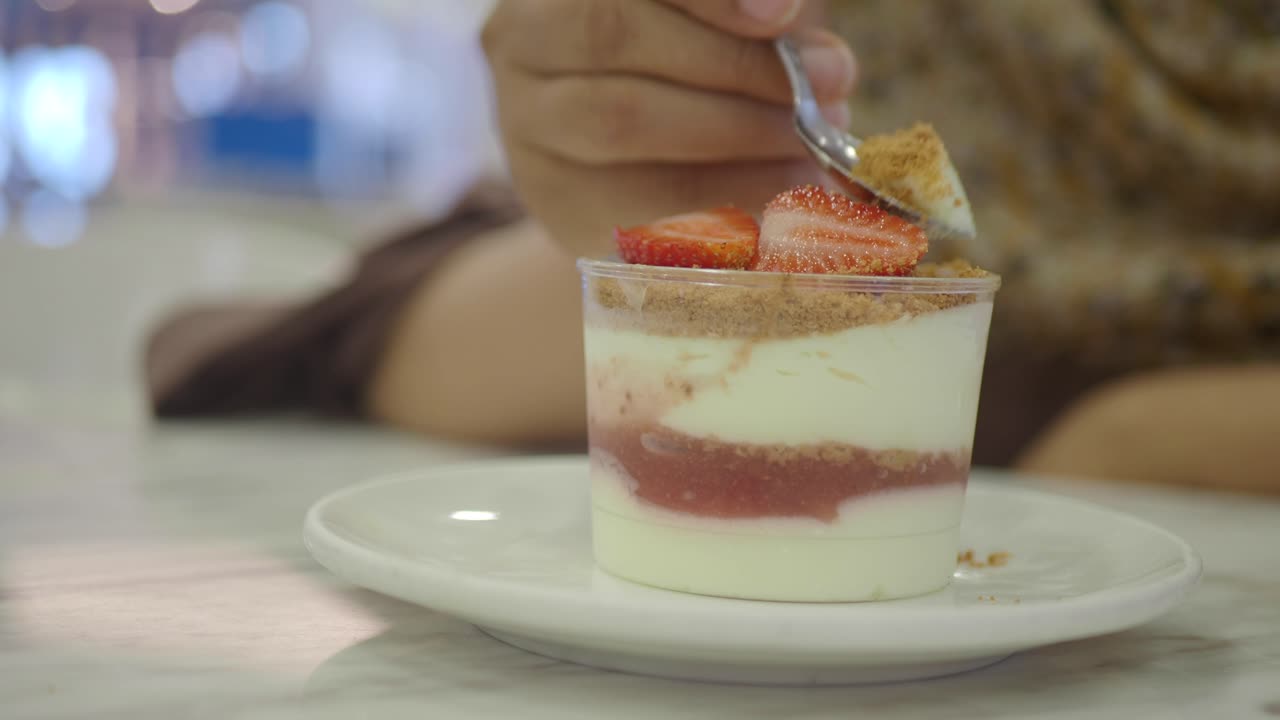 Person eating a small strawberry dessert