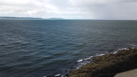 Aerial-shot-of-waves-crashing-against-rocky-shoreline-on-a-windy-day-in-Bangor,-Northern-Ireland