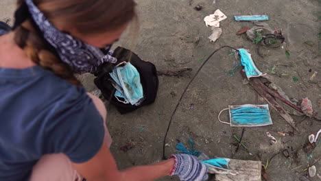 una mujer recogiendo desechos ambientales de una playa con mascarillas covid-19 usadas y desechadas