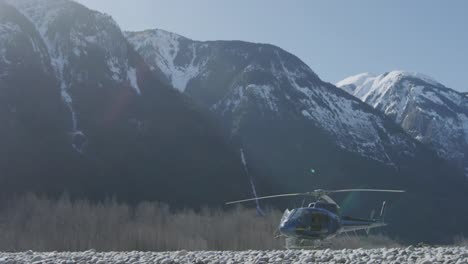 blue helicopter parked on rocky beach with snow capped mountains in the background 4k footage