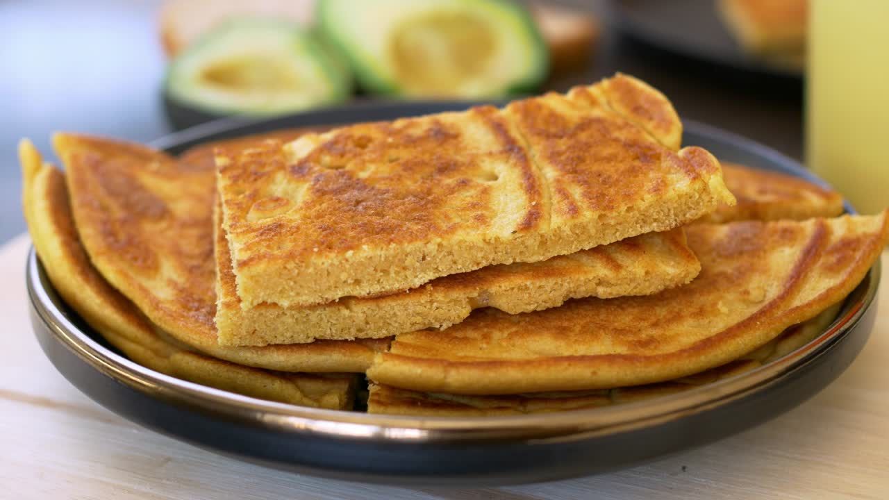 식탁에서 아침 식사를위한 팬케이크 클로즈업, 스파라의 도움으로 하나를 가져가십시오. 아침에 건강한 아침 식사, 전면에 맛있는 토르라, 배경에 흐릿한 아보카도