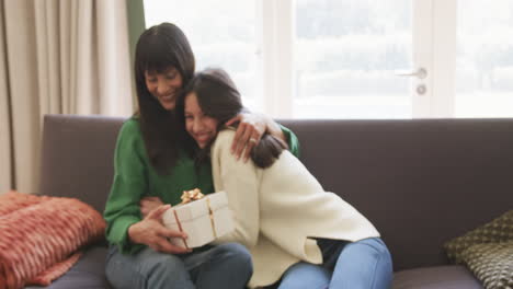 happy biracial mother and adult daughter exchanging christmas gift and hugging, slow motion