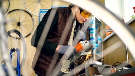 busy young man skilled repairman is working with electric circular saw at small metal part. bicycle spares and nice workshop interior are visible.