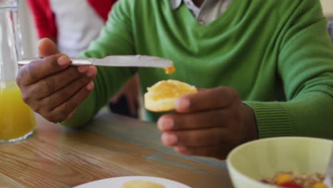 Afroamerikanischer-älterer-Mann,-Der-Beim-Frühstück-Mit-Der-Familie-Zu-Hause-Marmelade-Auf-Sein-Brot-Aufträgt