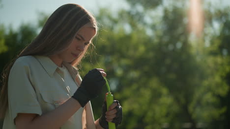 mujer enfocada se encuentra examinando la bomba de aire verde, profundamente en el pensamiento, contra un fondo sereno de árboles exuberantes y la luz del sol moteada en un día brillante