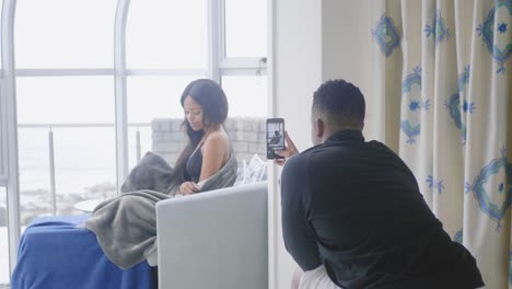 african american man filming his girlfriend on his apartment sofa with his cellphone